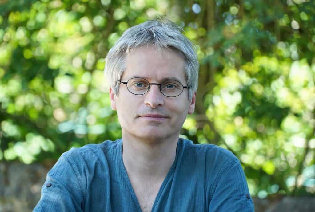 Immagine di Alexandre Mourot, regista, in un ambiente naturale con sfondo verde.